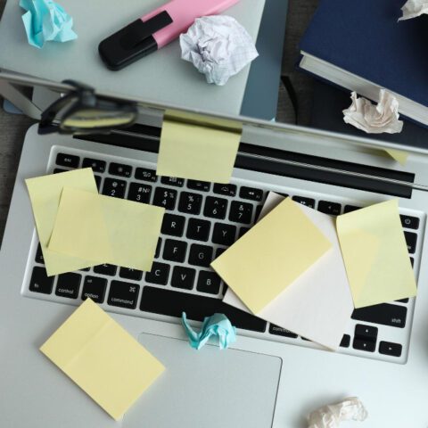 A stressed office worker looks overwhelmed while sitting at a desk cluttered with messy paperwork and files.