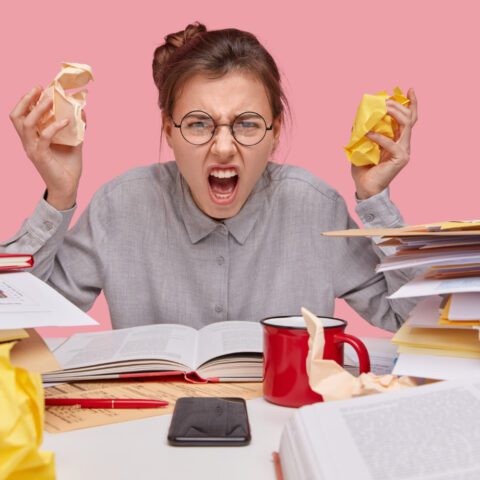 Stressed office worker at a desk overwhelmed by towering piles of paperwork and documents.